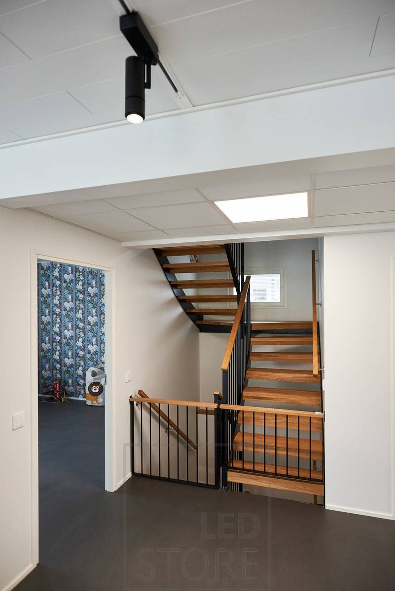 Des luminaires sur rail à leds noirs éclairent l'espace avec un éclairage directionnel, avec un grand panneau lumineux devant les escaliers. Ledstore.fi